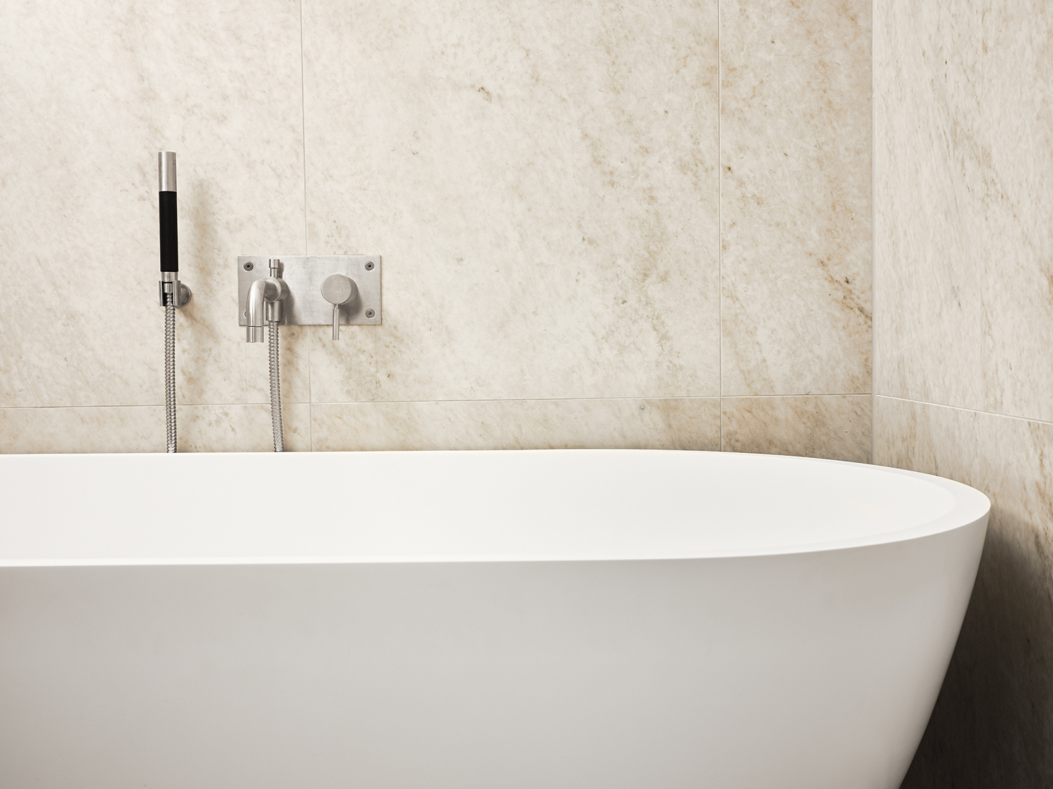 Varme toner i marmorfliser fra Bricmate på badet. Frittstående badekar.
